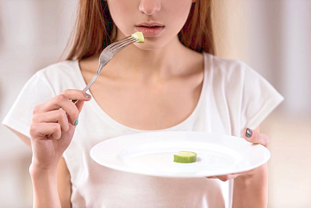 Vrouw proeft komkommerstukje met vork, houdt bord vast, close-up van mond en handen. ze heeft een eetstoornis, anorexia en ze vind eten heel erg moeilijk.