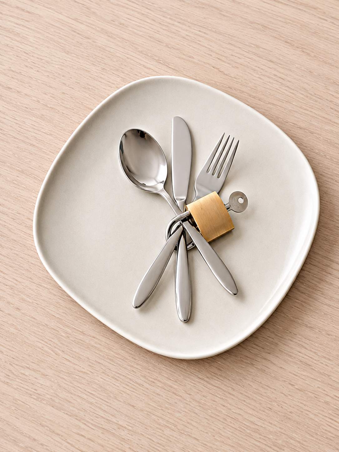 Bestekset op beige bord: lepel, mes en vork met gouden slot op houten tafel.
