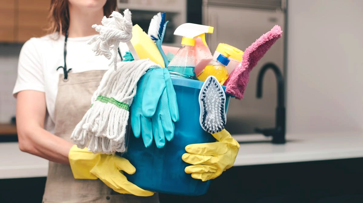 Persoon draagt schoonmaakmiddelen en handschoenen, met stofdoek en borstels voor het reinigen van een voertuig.
