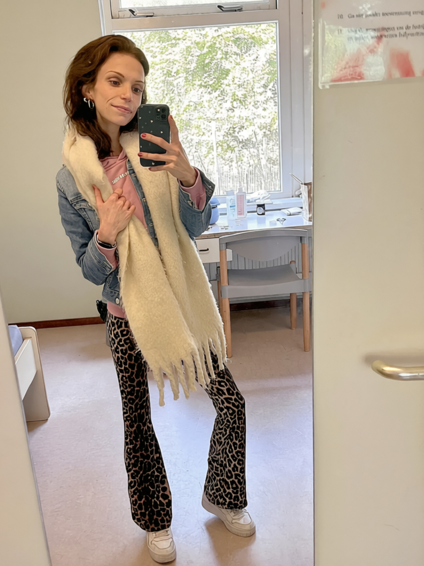 Vrouw maakt spiegelselfie in badkamer, draagt spijkerjas, roze top, beige sjaal en luipaardprint laarzen. opname eetstoorniskliniek