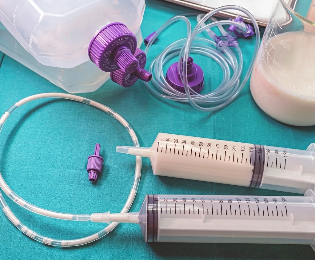 Medische spuiten en slangen op turquoise ondergrond, met paarse aansluitingen en maatverdeling voor vloeistofdosering. Sondevoeding. Bolussen. Shots. Opname PAAZ ziekenhuis psychiatrie, gewichtsherstel, sondevoeding, beroerd, eetstoornis, anorexia