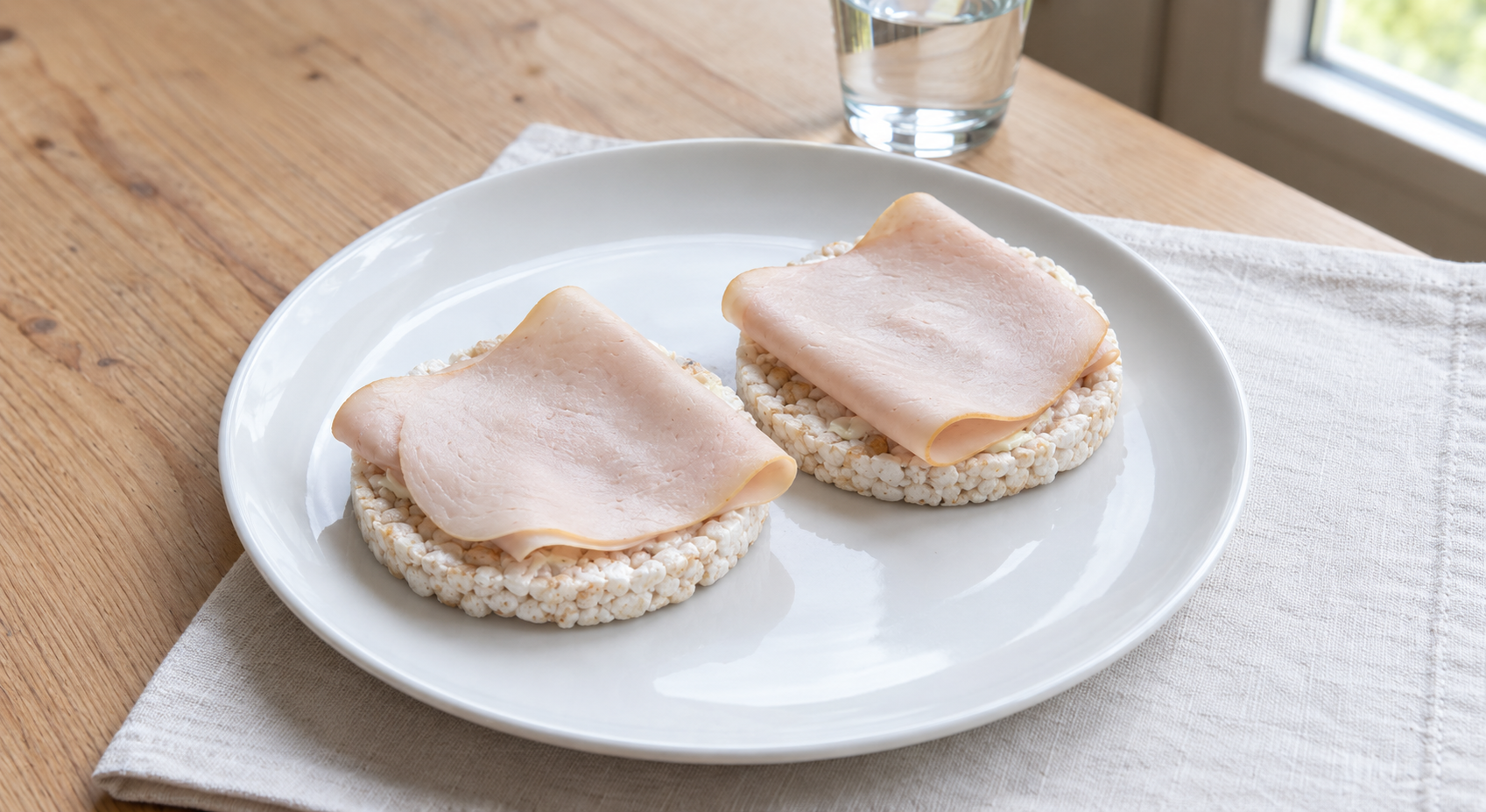 Twee rolletjes met rijst en ham op een wit bord, naast een glas water op tafel.