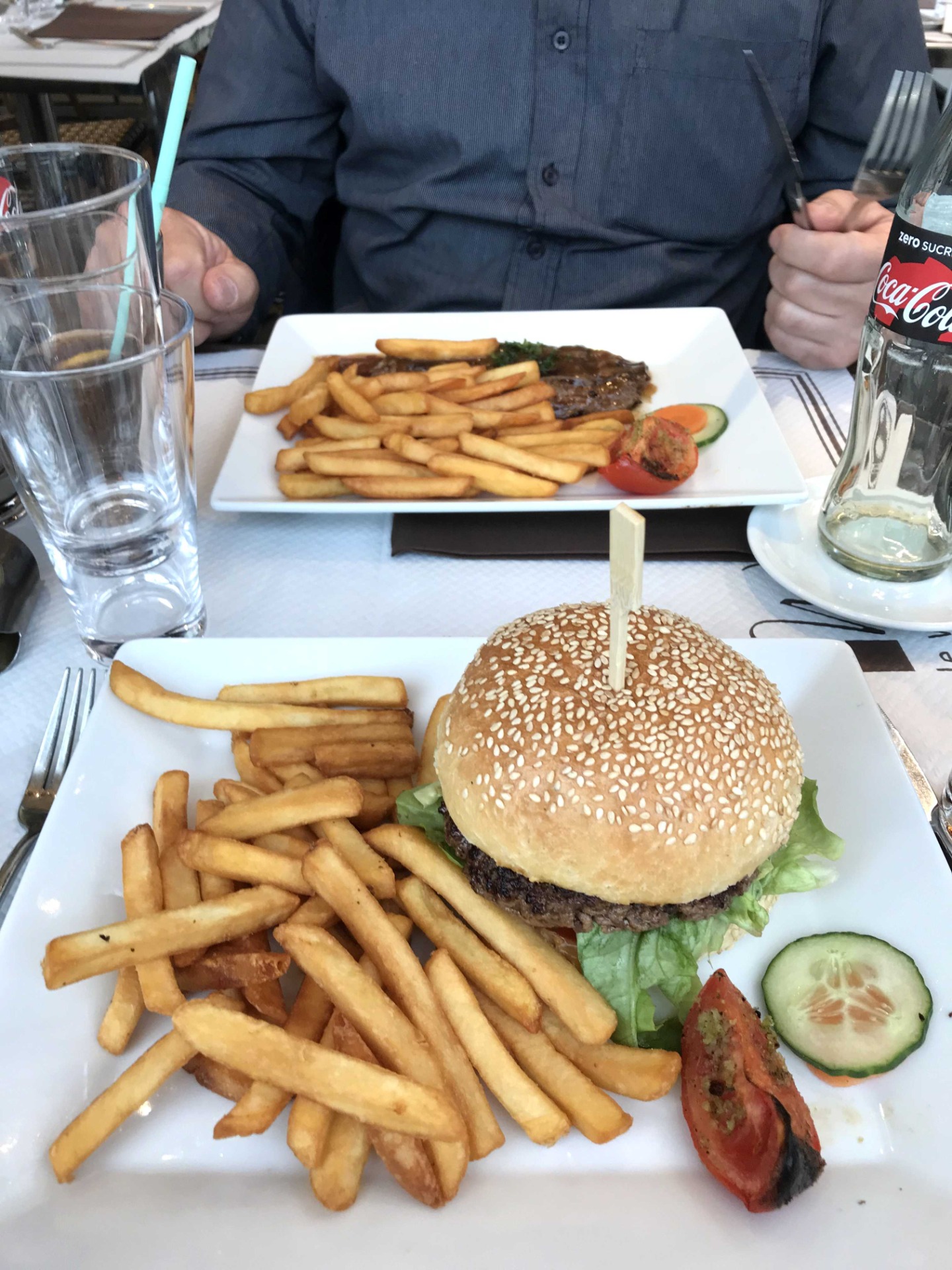 Borden met friet en hamburger, glazen water en frisdrank, handen aan tafel met bestek. Restaurant uiteten, diner met een eetstoornis