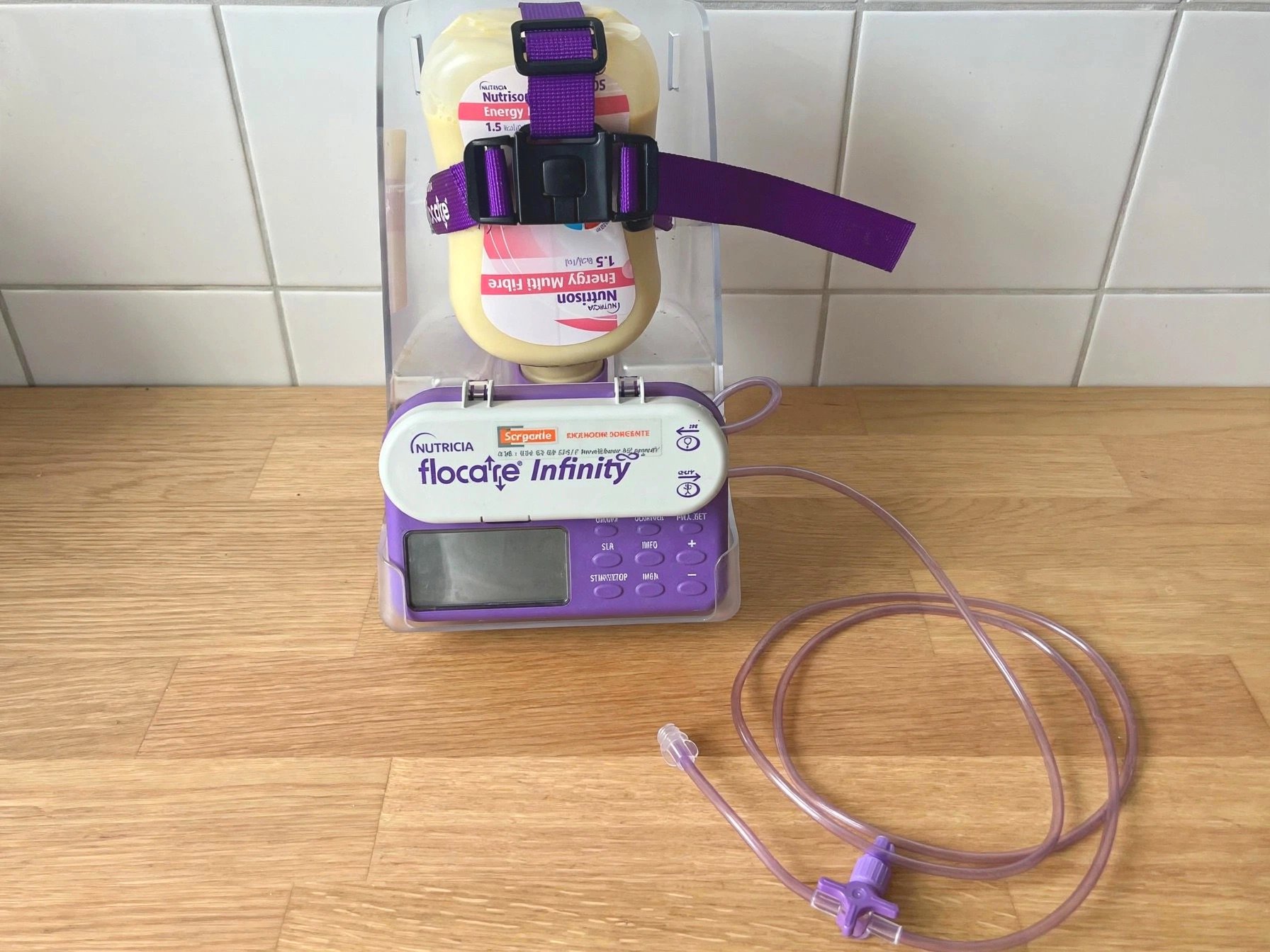 Medische voedingspomp Nutricia flocare infinity met paarse slang en display op houten vloer.