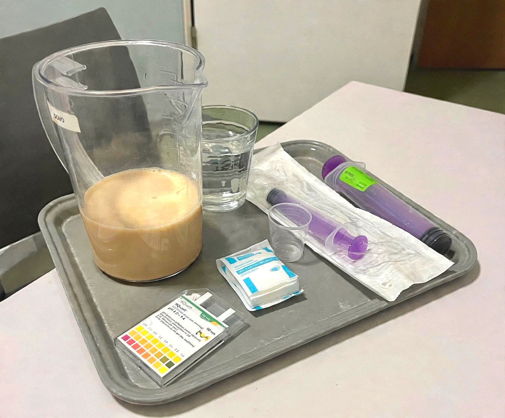 Laboratoriumtray met maatbekers, bekerglas met vloeistof, teststrookjes, handschoenen en paarse pipet op tafel.