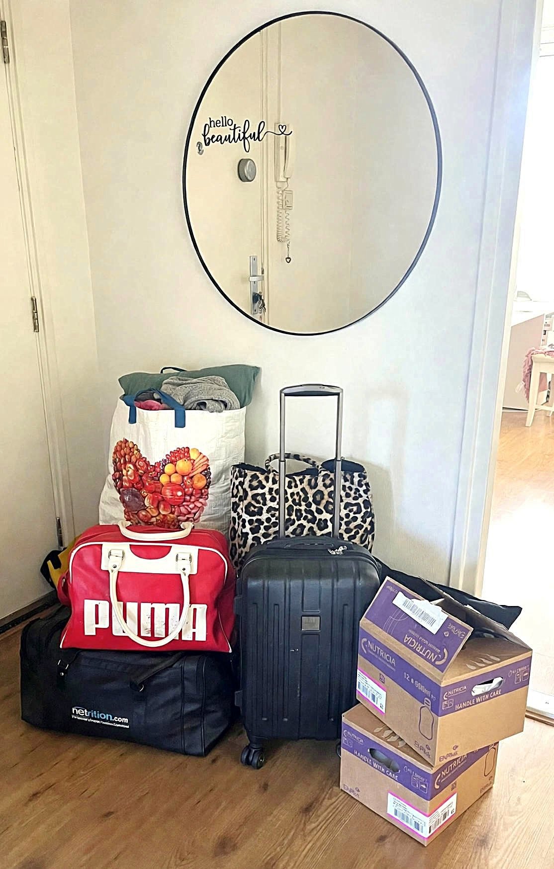 Ronde spiegel boven stapel koffers en tassen, met dozen en boodschappen op de vloer in een kamer. Dozen met sondevoeding. Opname ziekenhuis op de MPU.